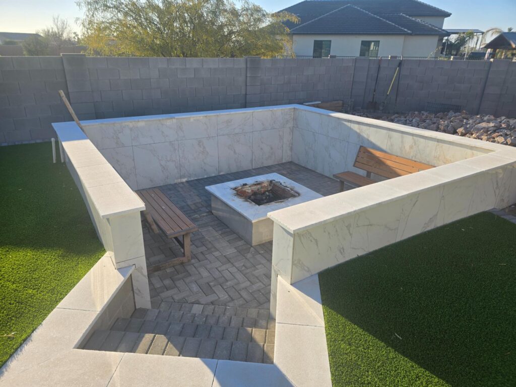 Finished sunken fire pit lounge with marble tile and wood benches at Mesa residence