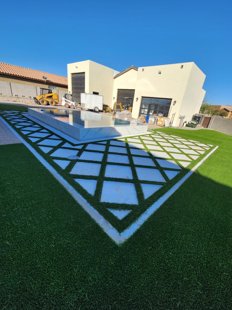 Geometric turf and tile layout surrounding raised pool during backyard build