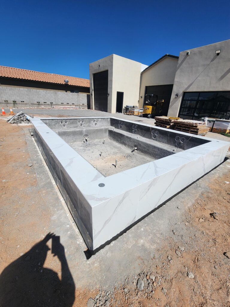 Pool shell installation in progress with marble coping and construction equipment